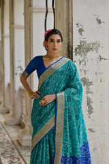 Woman wearing a teal saree with a blue blouse in an indoor setting.