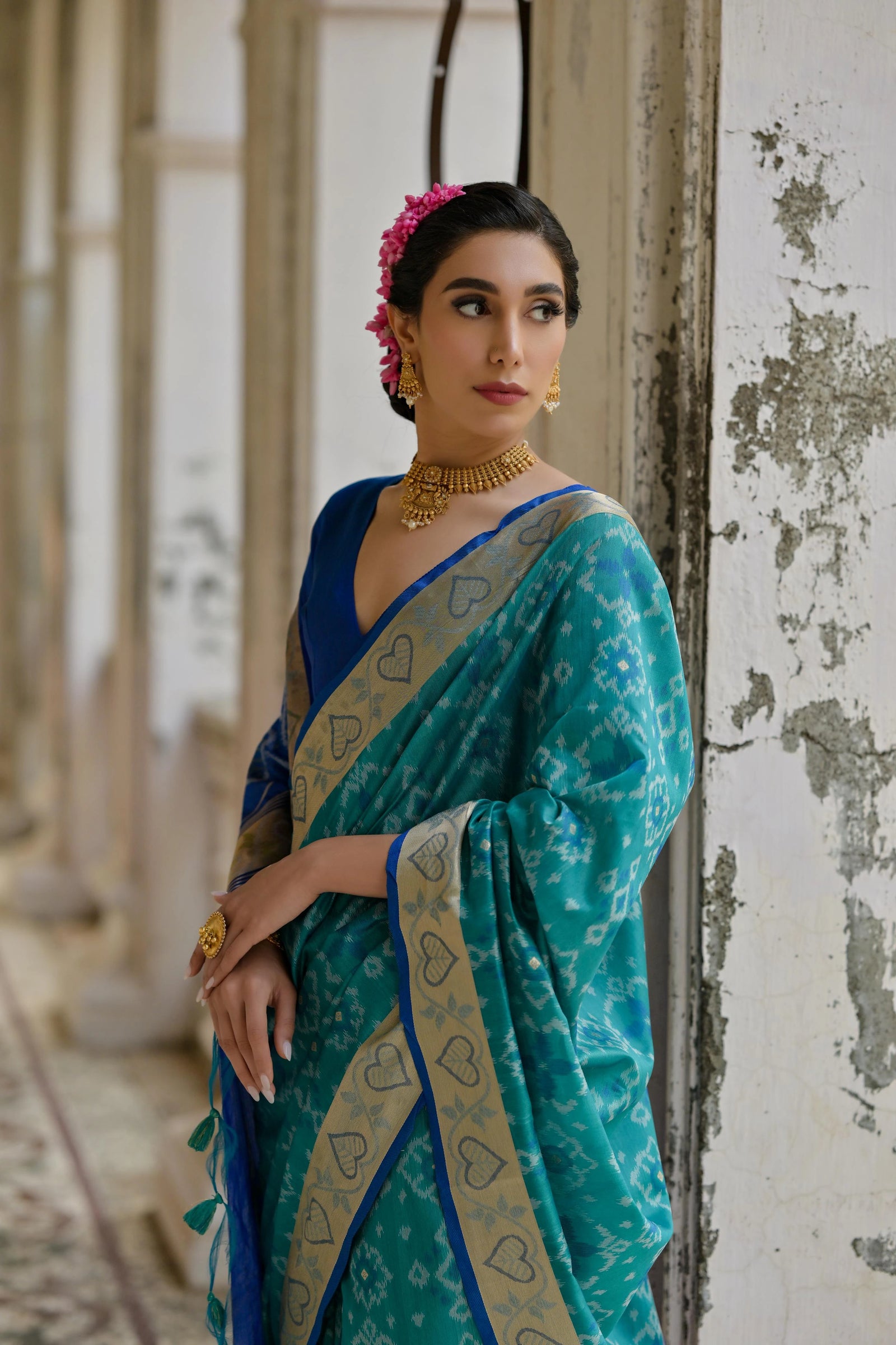 Woman in a blue and green saree with floral hair accessories in an indoor setting.