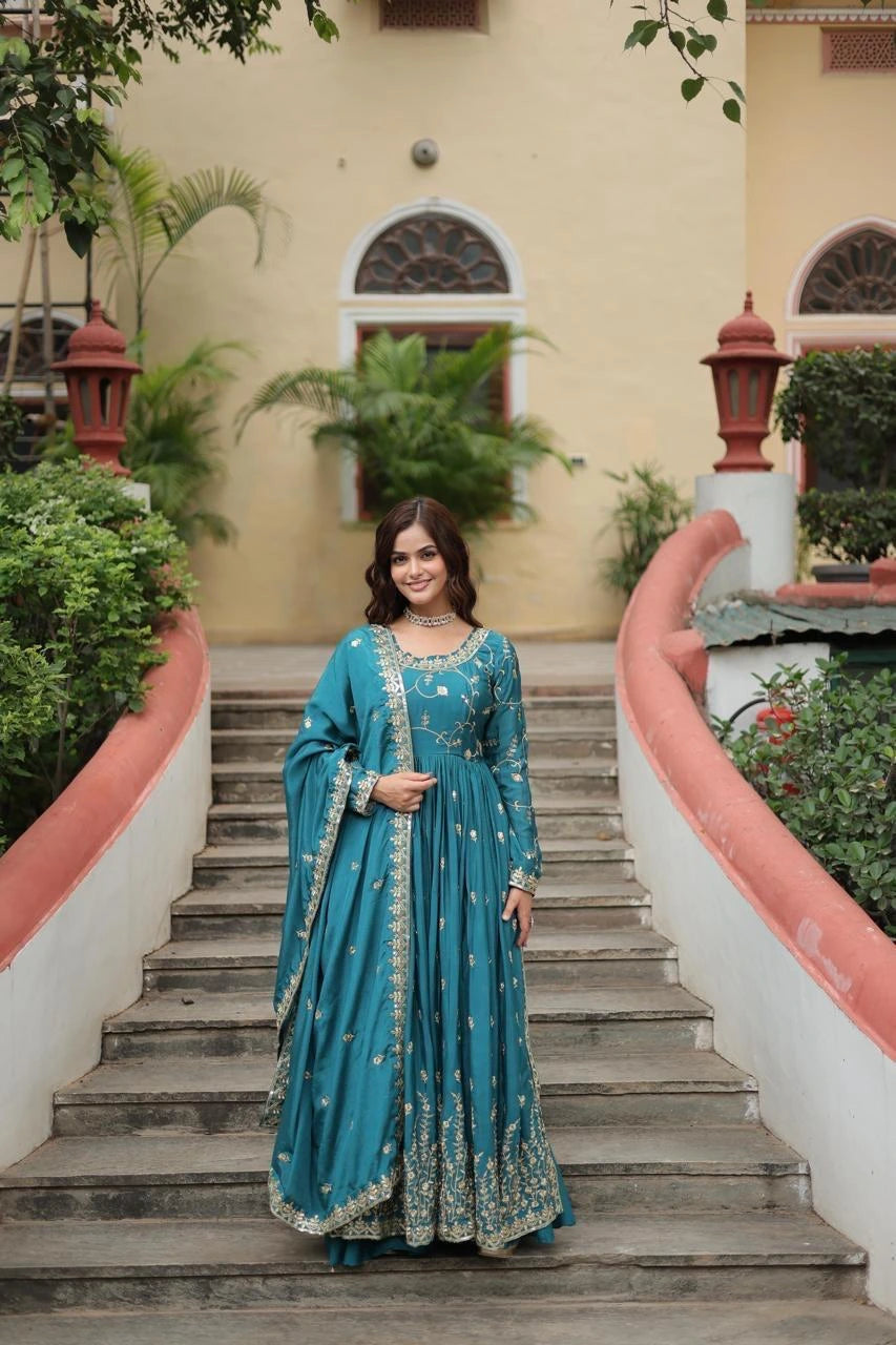Woman in a blue traditional outfit standing on stone steps with greenery and a building in the background