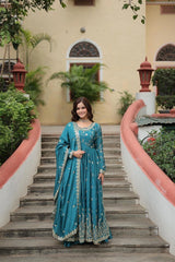 Woman in a blue traditional outfit standing on stone steps with greenery and a building in the background