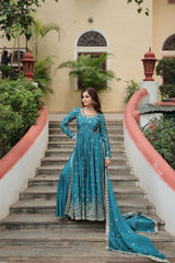 Woman in a blue traditional outfit standing on a staircase with a building and greenery in the background