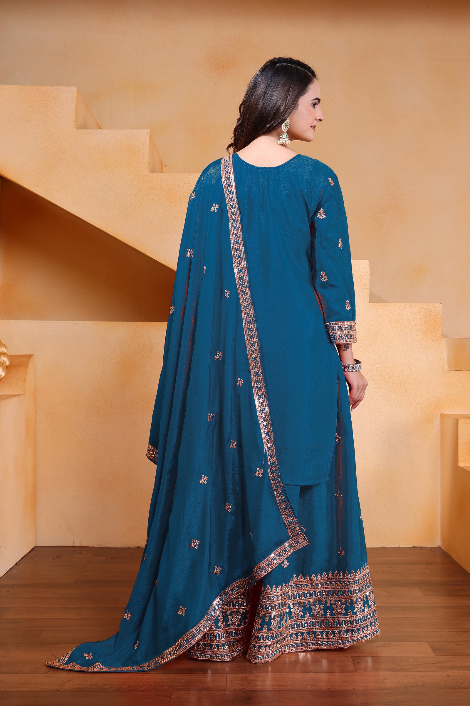 Woman wearing a blue traditional outfit with intricate patterns in an indoor setting.