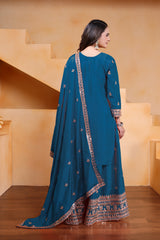 Woman wearing a blue traditional outfit with intricate patterns in an indoor setting.