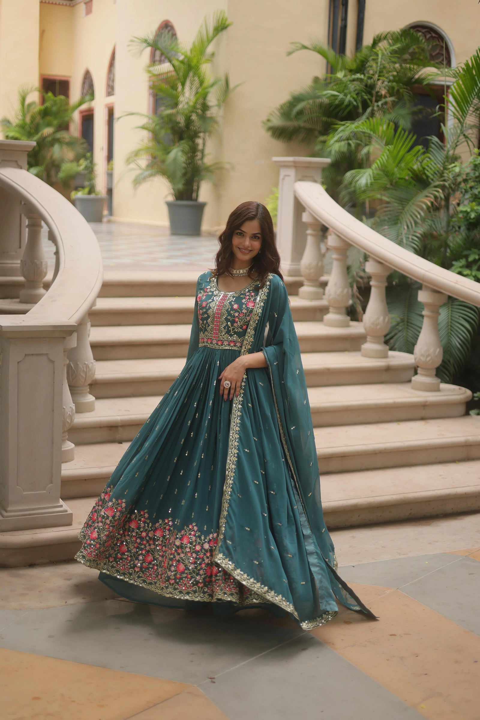 Woman in a teal traditional outfit standing on steps with greenery in the background