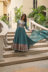 Woman in a teal dress with floral patterns standing on stone steps outdoors.