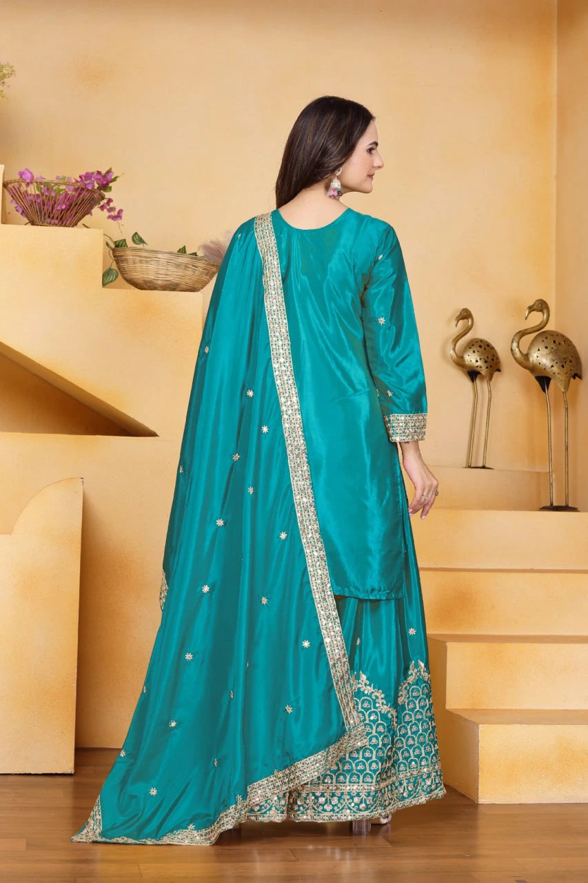 Woman in a teal traditional outfit with gold embroidery standing in a decorative setting.