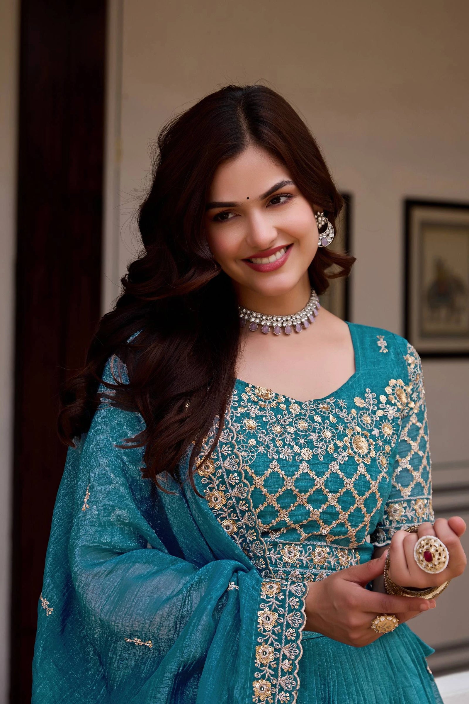 Woman in a blue embroidered traditional outfit with jewelry indoors.