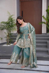 Woman in a teal traditional outfit with gold embroidery standing on steps outdoors.