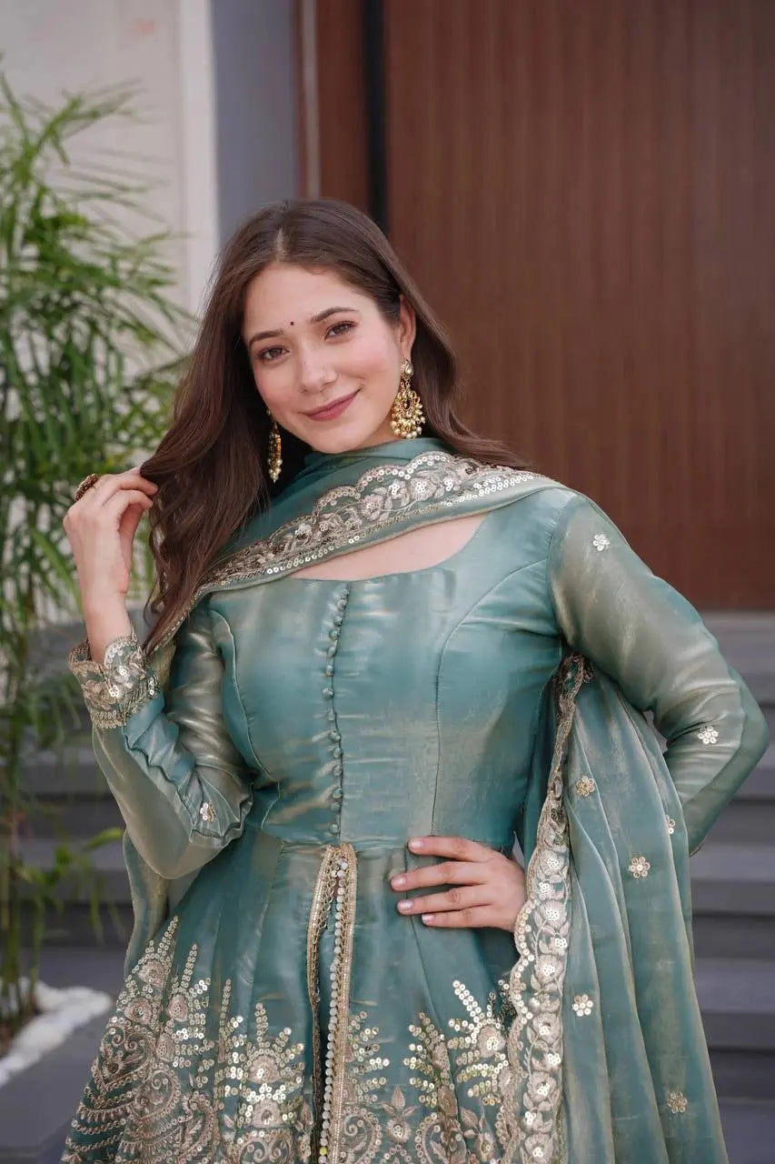 Woman in a traditional green outfit with gold embroidery standing outdoors.