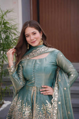 Woman in a traditional green outfit with gold embroidery standing outdoors.
