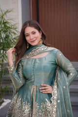 Woman in a traditional green outfit with gold embroidery standing outdoors.
