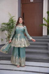 Woman in a teal traditional outfit with gold embroidery standing on steps.