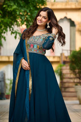 Woman in a traditional blue outfit with intricate patterns, standing outdoors.