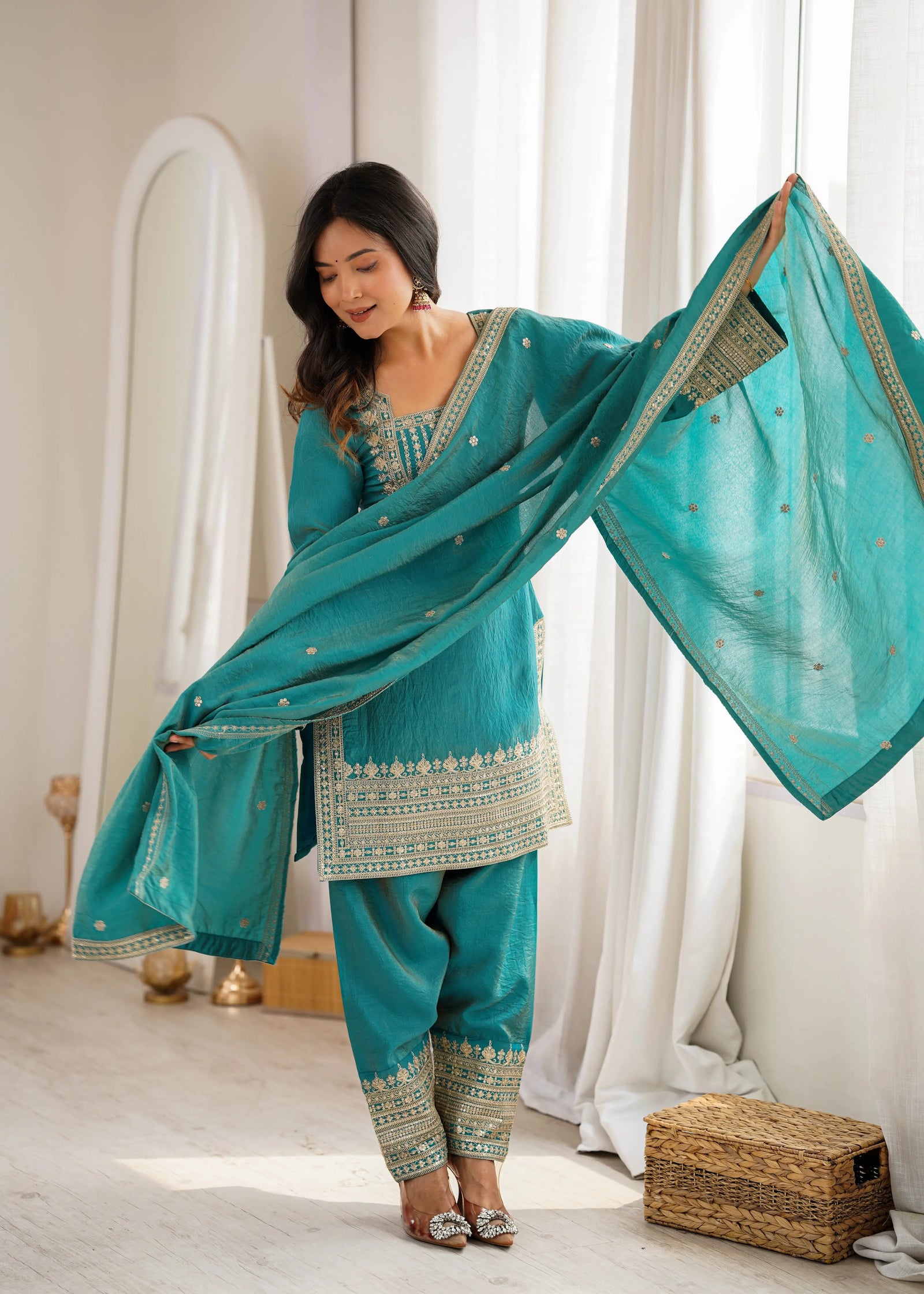 Woman in a teal traditional outfit with matching dupatta in a bright room.