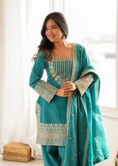 Woman wearing a teal traditional outfit with gold embroidery indoors.