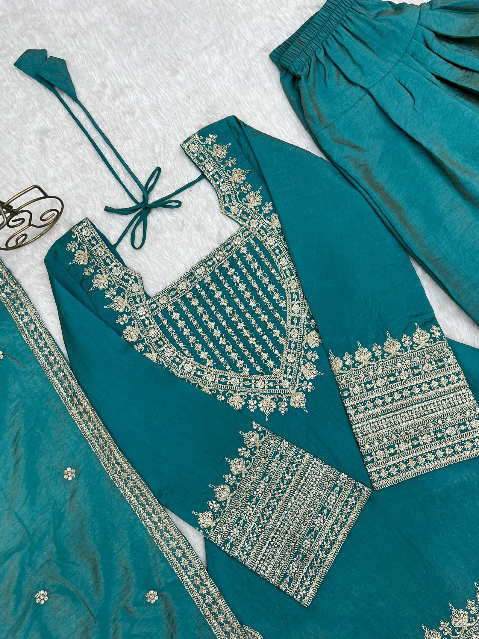 Teal traditional outfit with gold embroidery on a textured white background