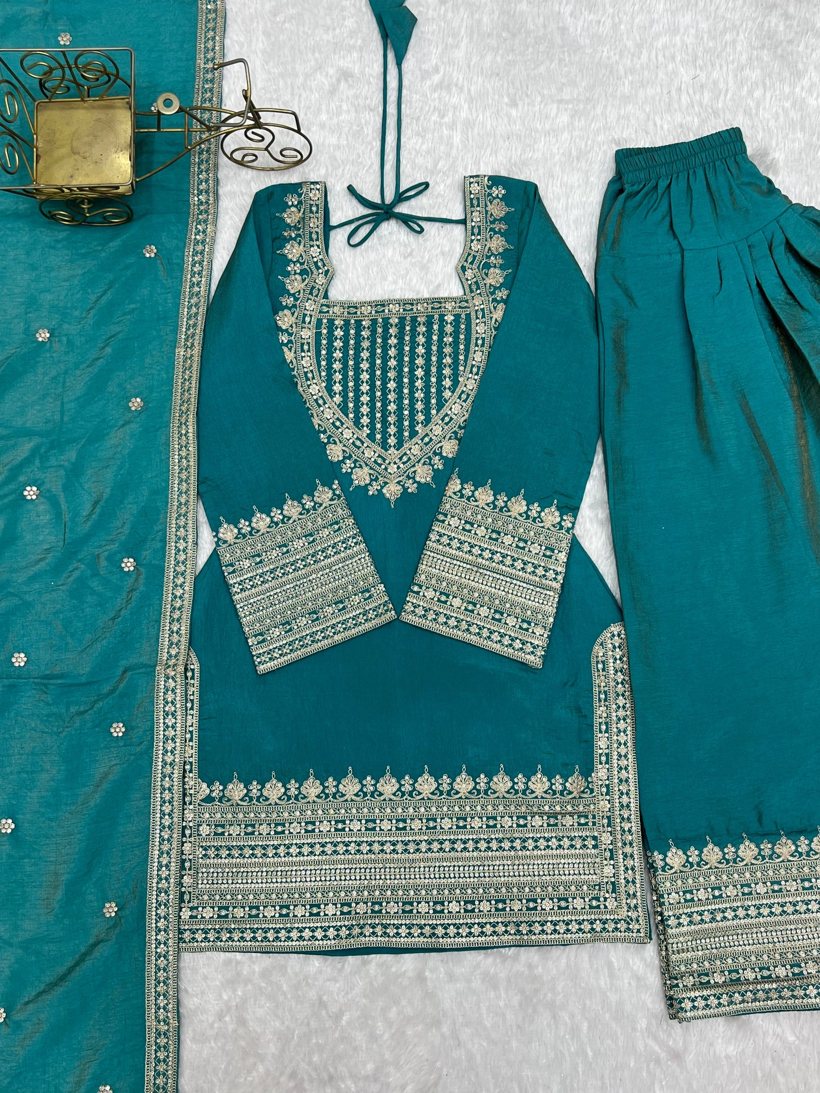Teal traditional outfit with intricate silver embroidery on a textured white background