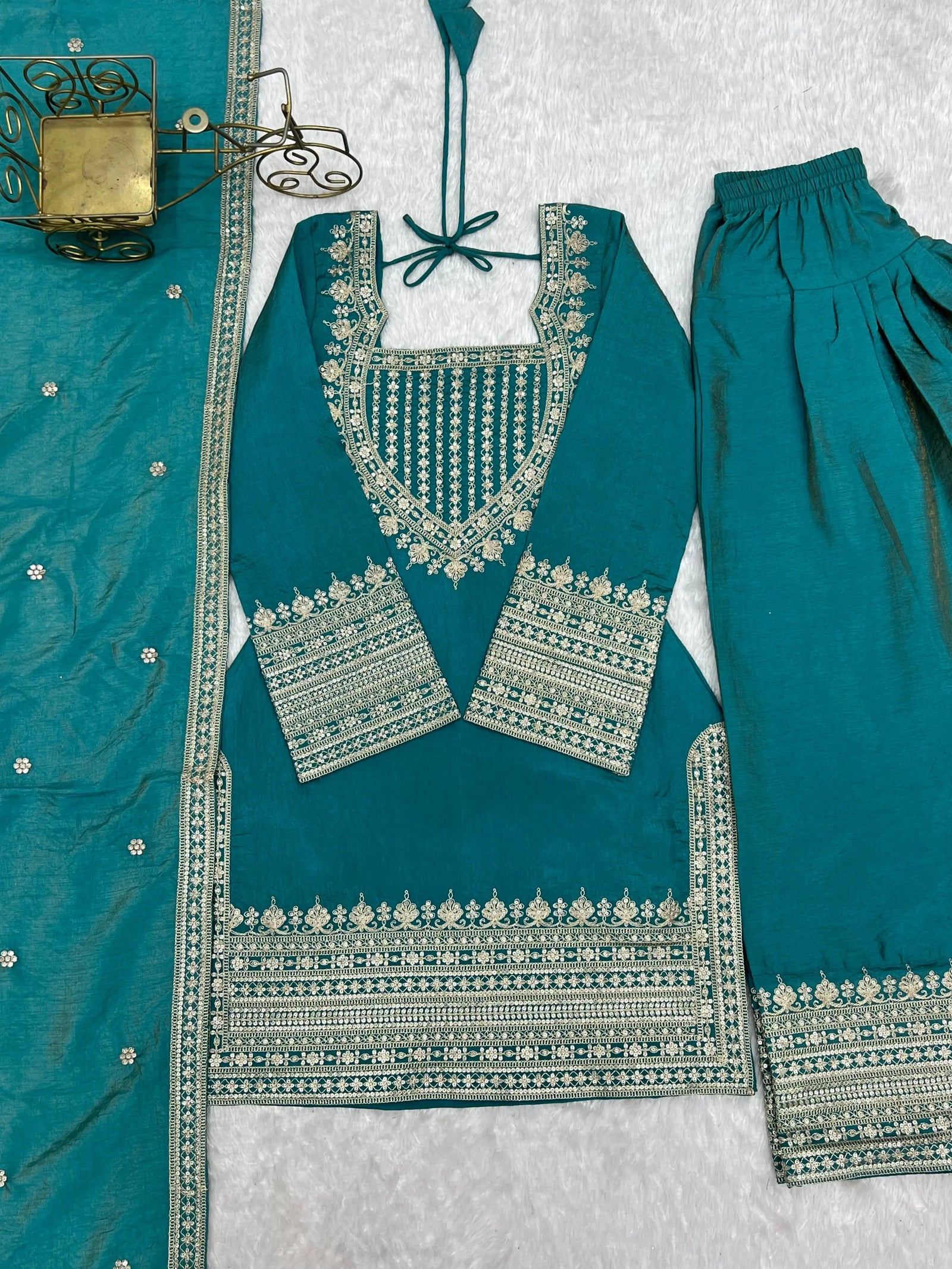Teal traditional outfit with intricate silver embroidery on a textured white background