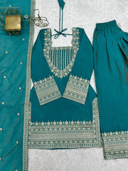 Teal traditional outfit with intricate silver embroidery on a textured white background