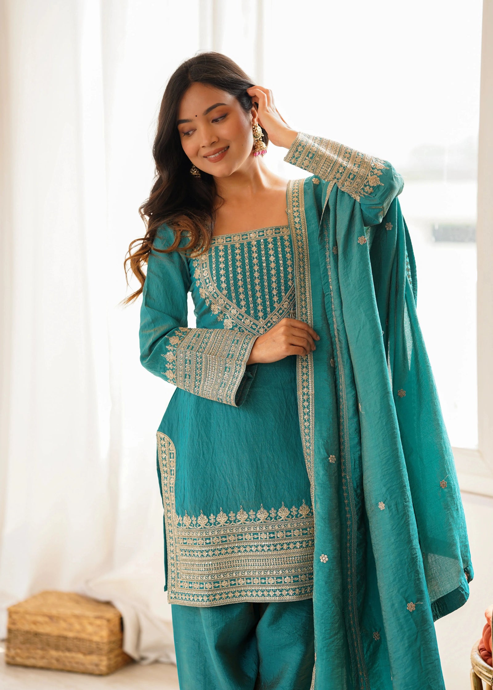 Woman wearing a teal traditional outfit with white embroidery indoors.