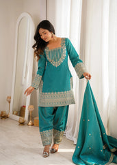 Woman in a teal embroidered traditional outfit holding a matching dupatta in a well-lit room.