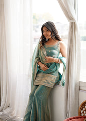 Woman in a teal saree with white patterns sitting by a window.