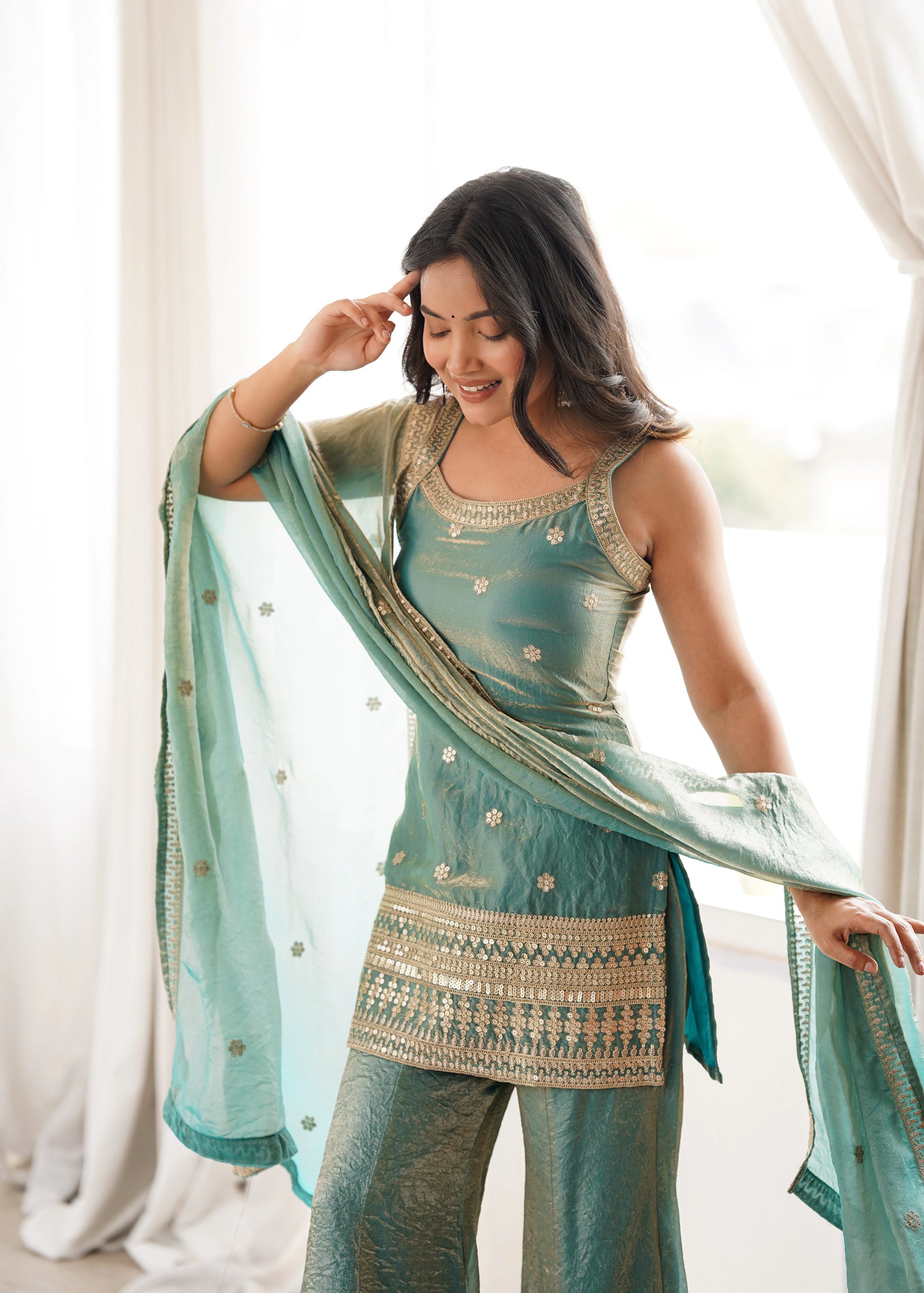 Woman wearing a traditional outfit with a green dupatta in a bright room.