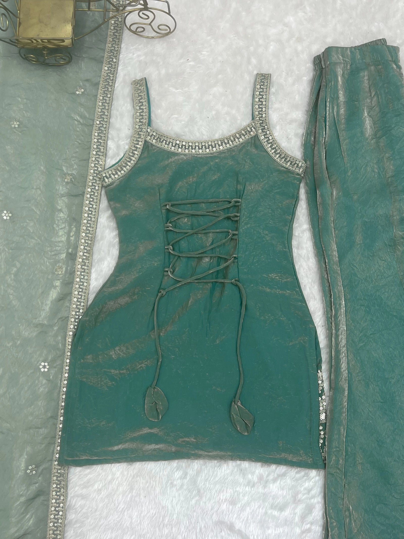 Teal outfit with lace-up front and decorative elements on a textured white background