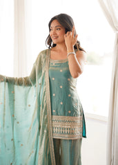 Woman wearing a light blue traditional outfit with a matching dupatta, standing indoors.