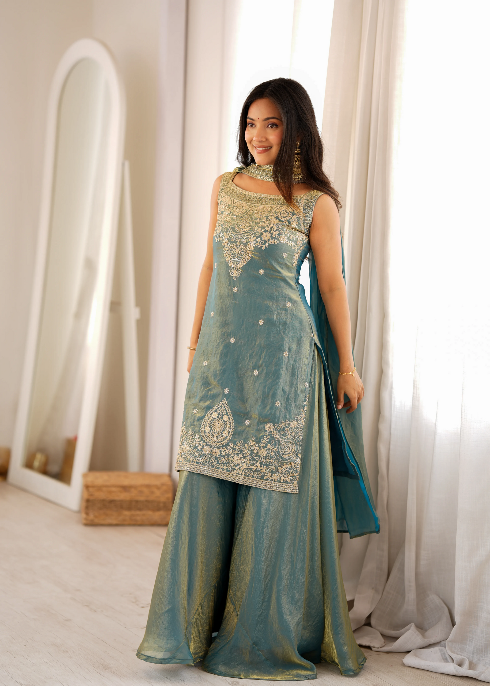 Woman wearing a traditional teal and gold outfit with white curtains in the background