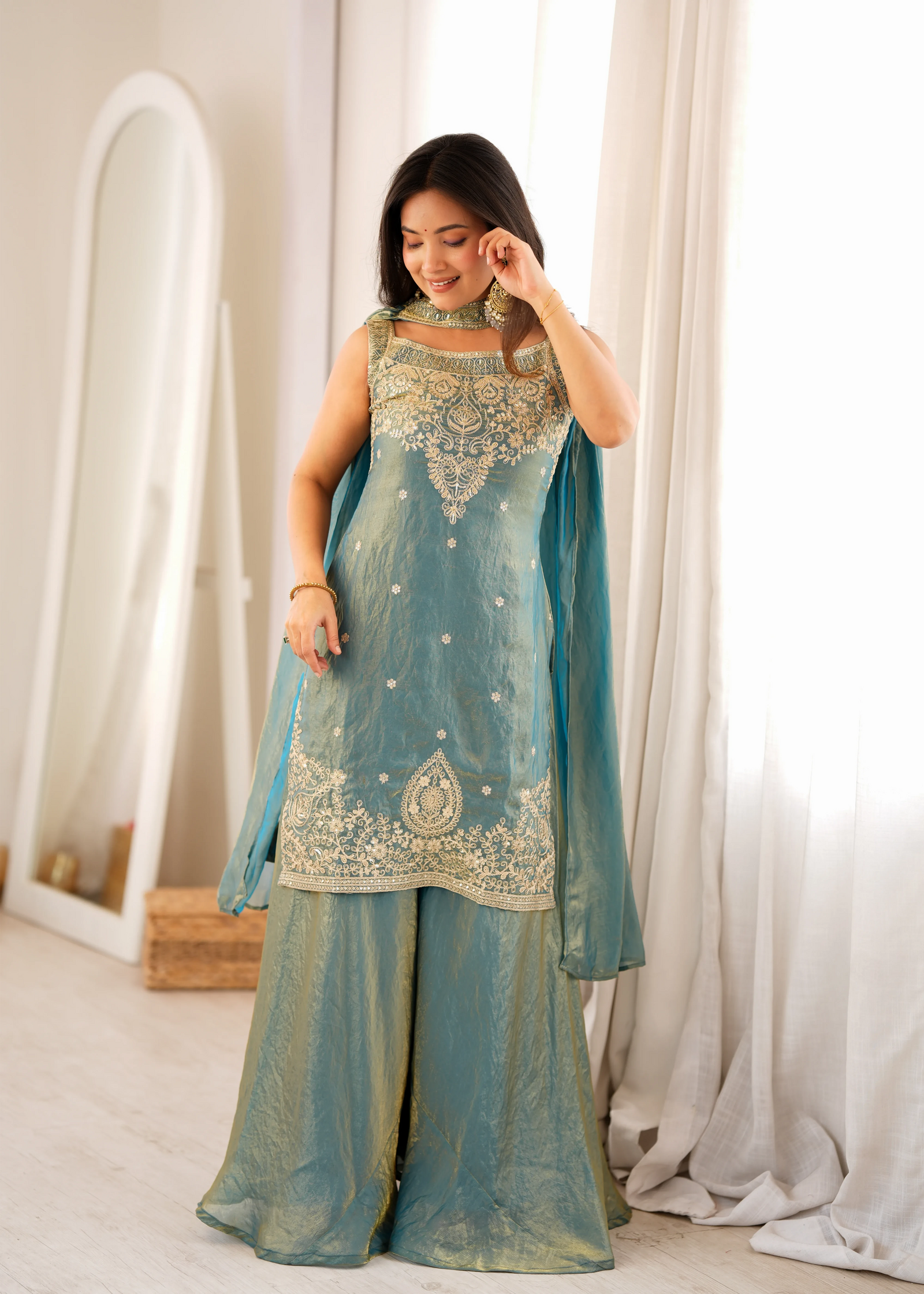 Woman wearing a traditional outfit with intricate designs in a bright room.