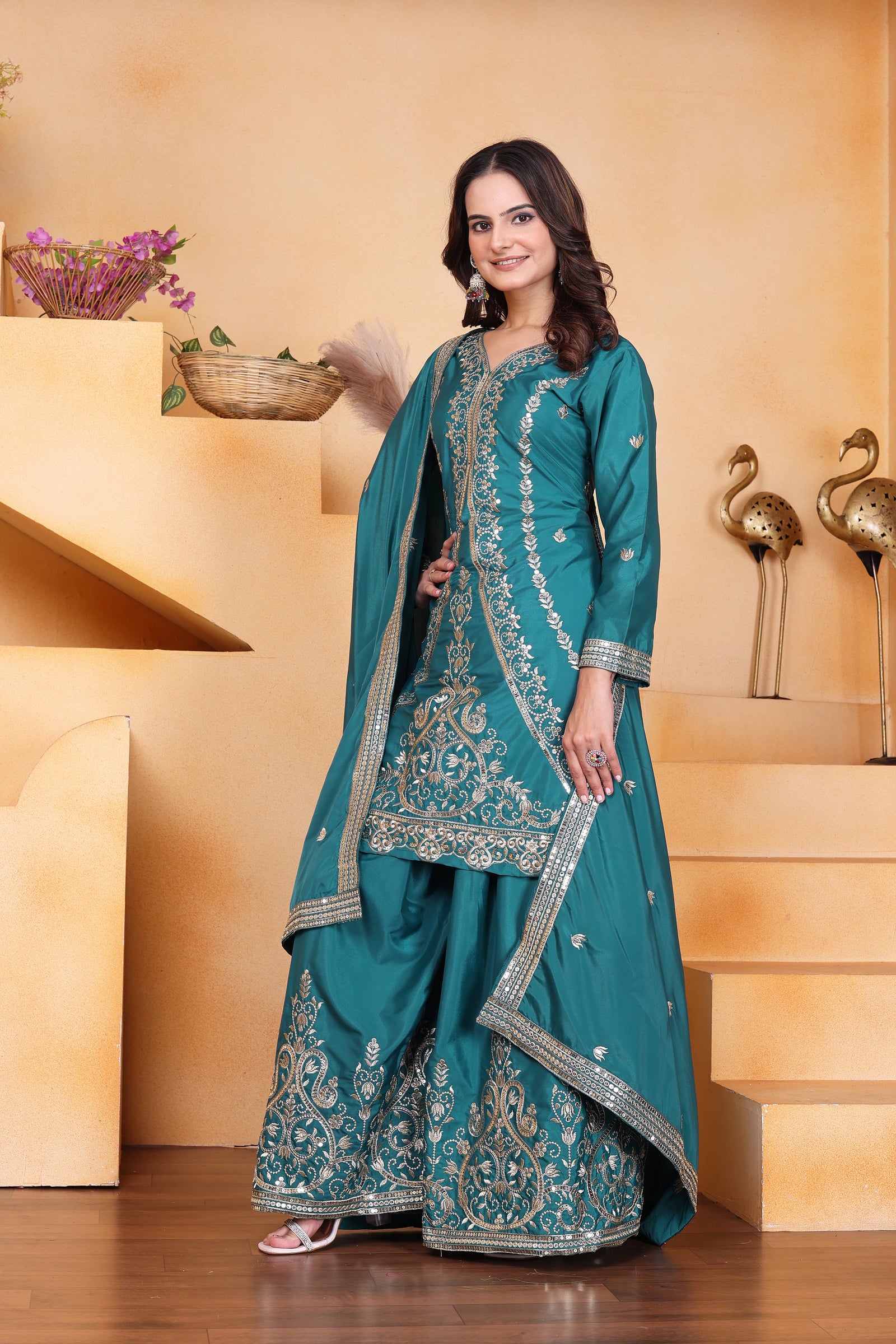 Woman in a teal embroidered traditional outfit standing on a staircase.