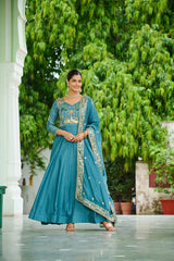 Woman in a blue traditional outfit standing outdoors with greenery in the background