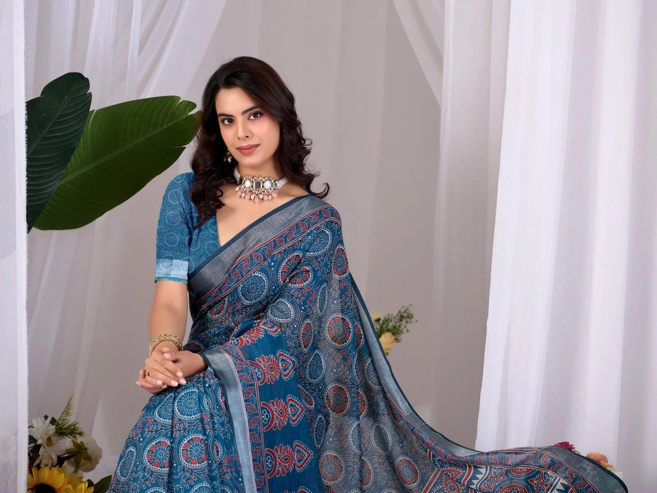 Woman wearing a blue saree with a white curtain and green leaves in the background