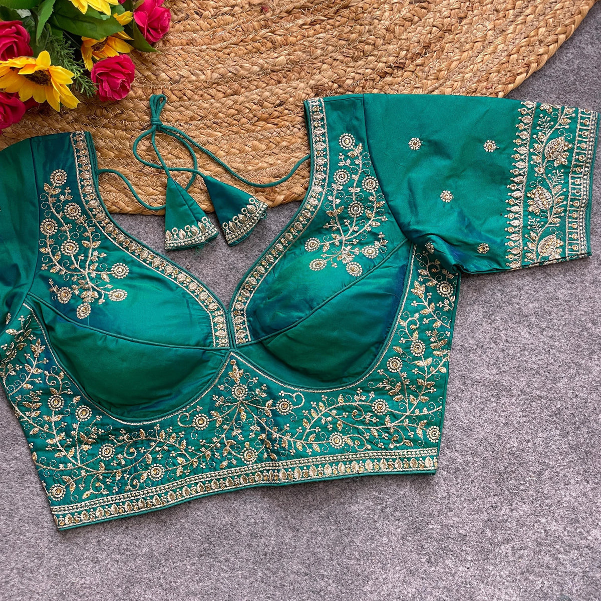 Green embroidered blouse on a textured surface with flowers in the background