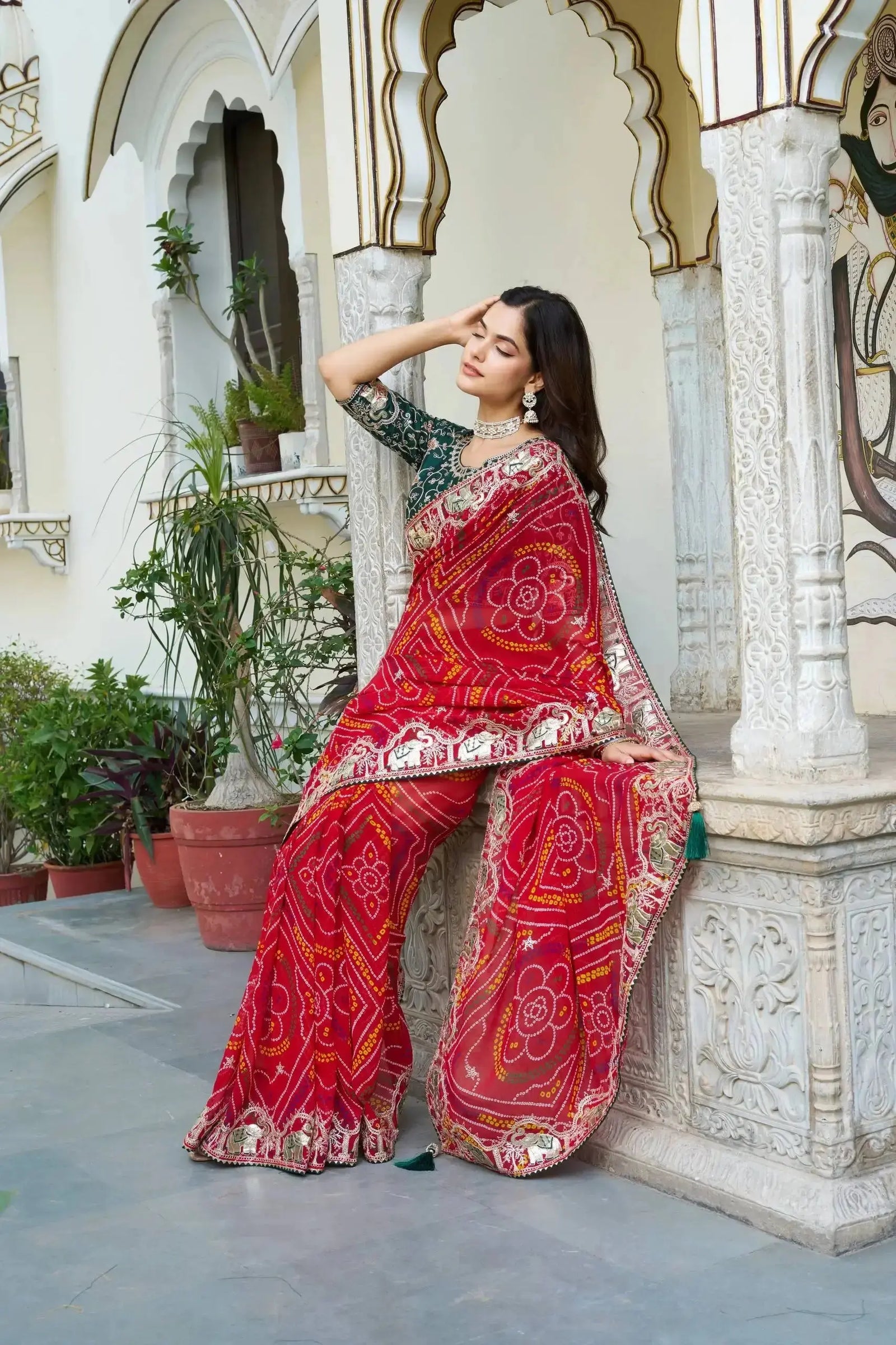 Model in Red Gota Patti Saree seated against carved palace column