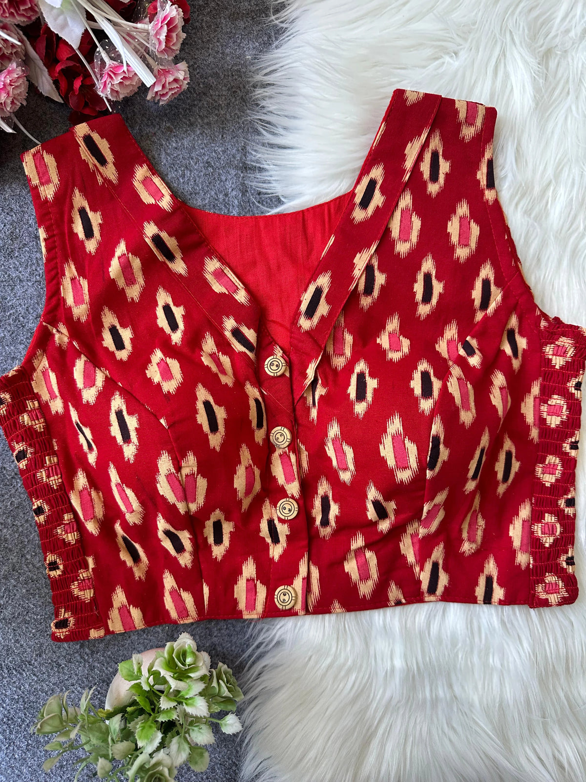 Red patterned top with buttons on a textured surface with flowers.