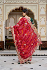Woman in a red saree with gold patterns in an ornate room.