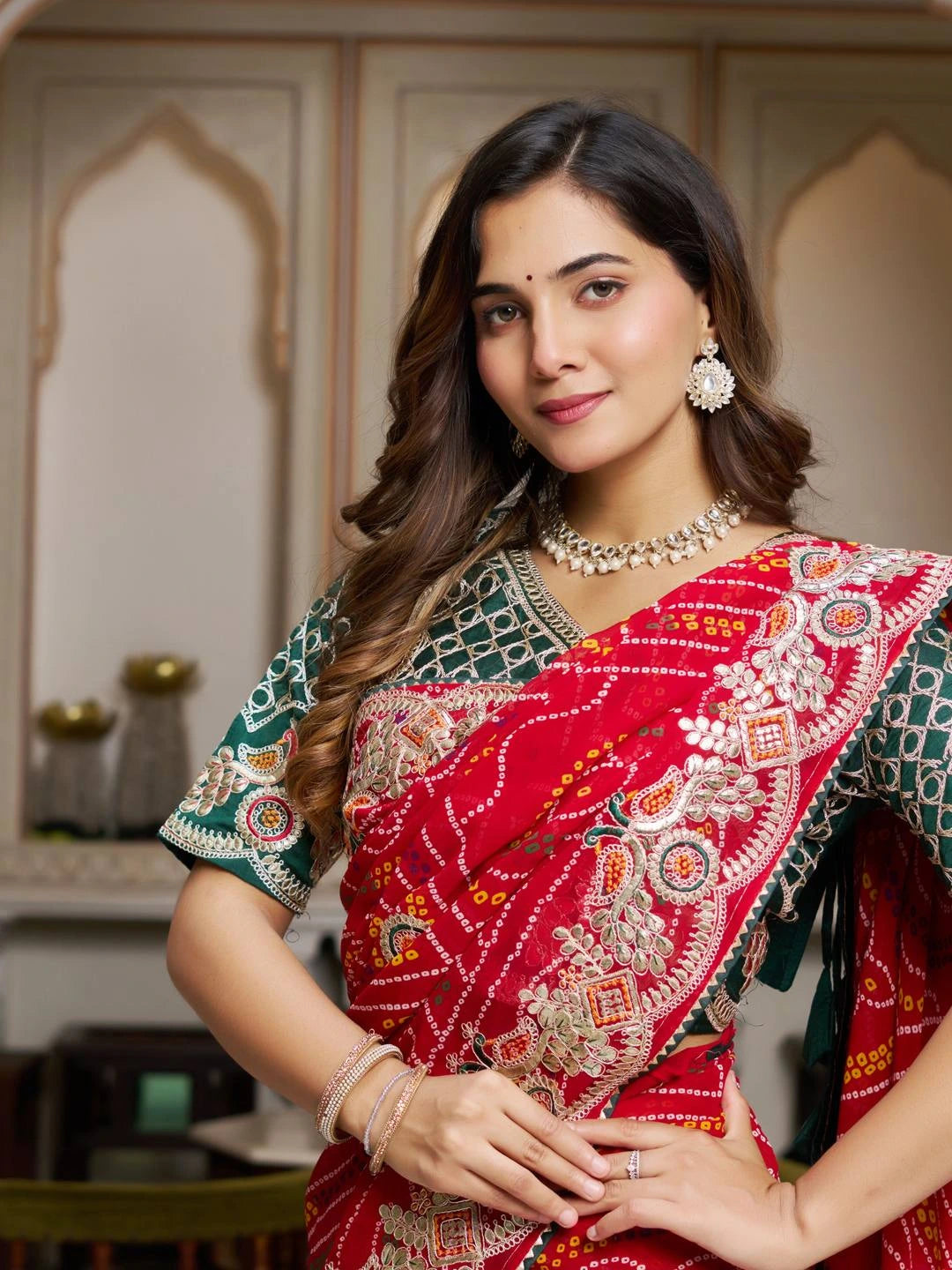 Woman wearing a traditional red and green saree with intricate patterns indoors.