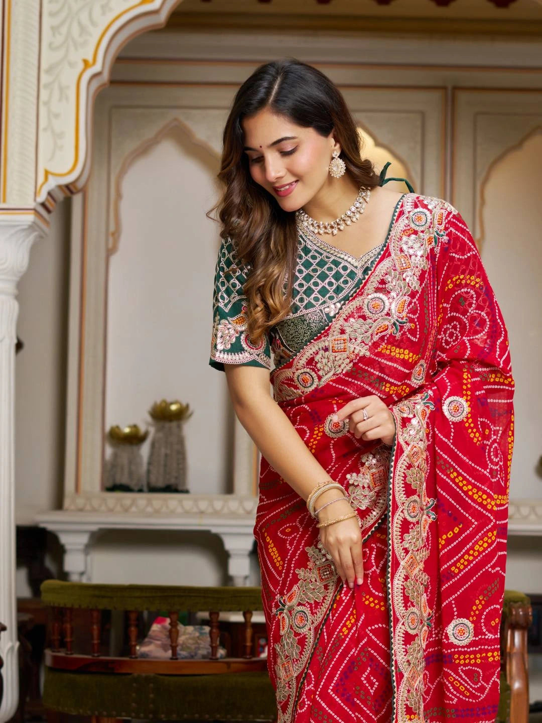 Woman in a red and gold saree with intricate patterns in an ornate room.