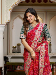 Woman wearing a traditional red and green saree with intricate patterns in an ornate room.