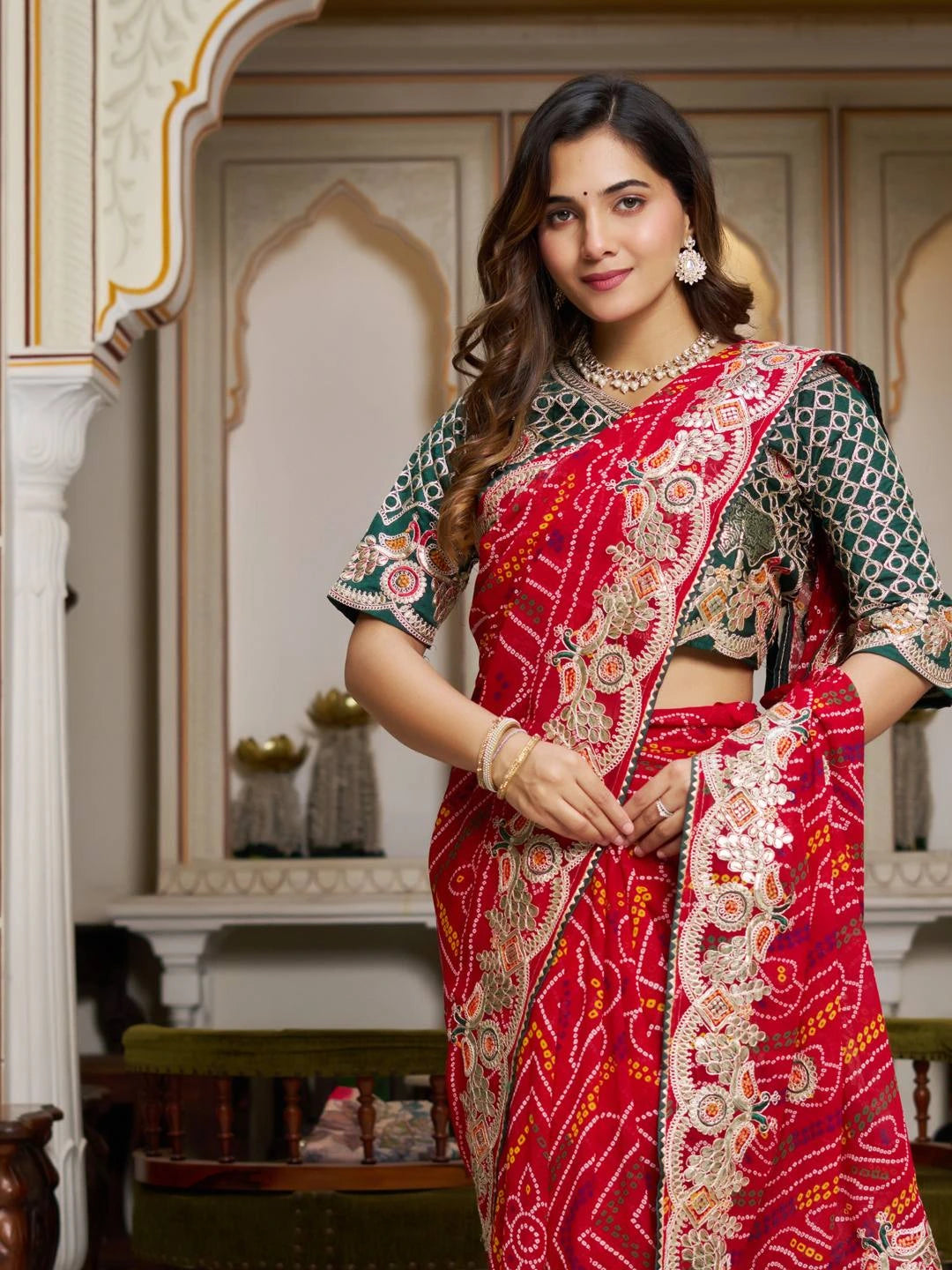Woman wearing a red and green saree with intricate patterns in an ornate room.