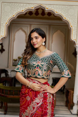 Woman wearing a traditional outfit with a green blouse and red saree in an ornate room.