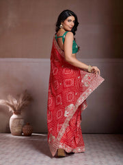 Woman wearing a red saree with white patterns against a neutral background