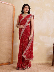Woman wearing a red saree with white patterns against a beige wall.
