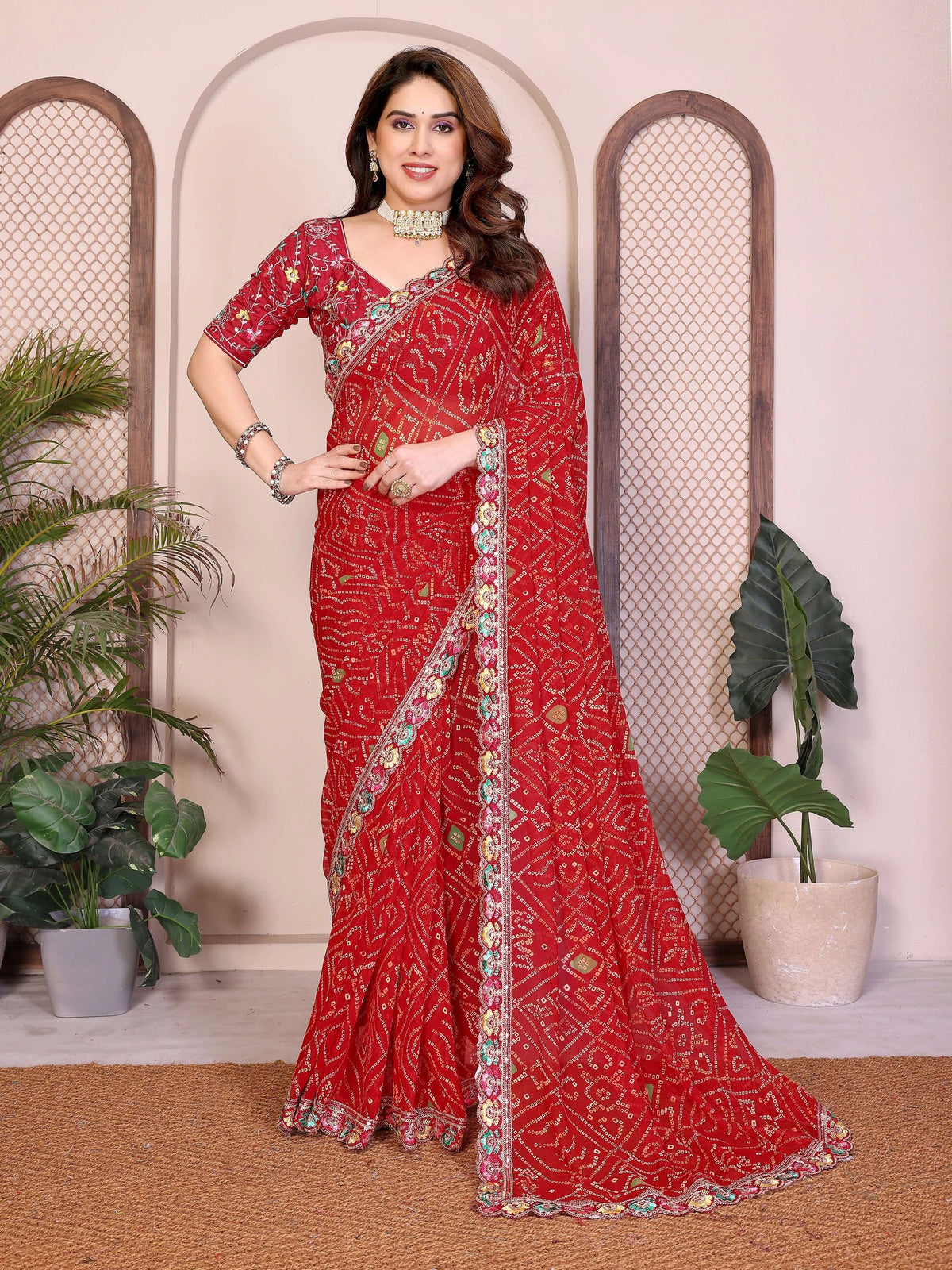 Woman wearing a red saree with intricate patterns in a decorative setting.