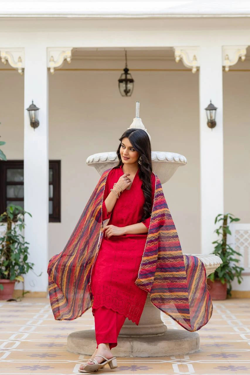 Woman in a red outfit with a colorful shawl standing in an elegant indoor setting.