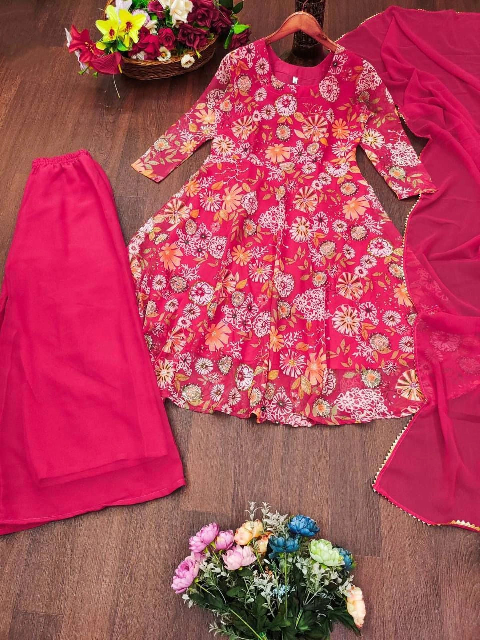 Pink floral dress with matching pants and dupatta on a wooden surface with flowers.