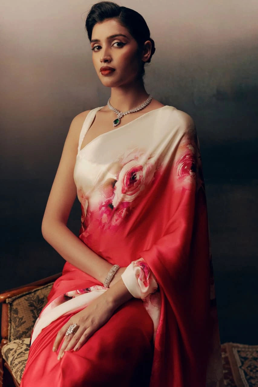 Woman wearing a red saree with floral patterns, sitting on a textured surface.