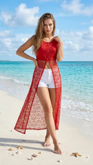 Woman in a red cover-up and white shorts standing on a beach with turquoise water and blue sky.
